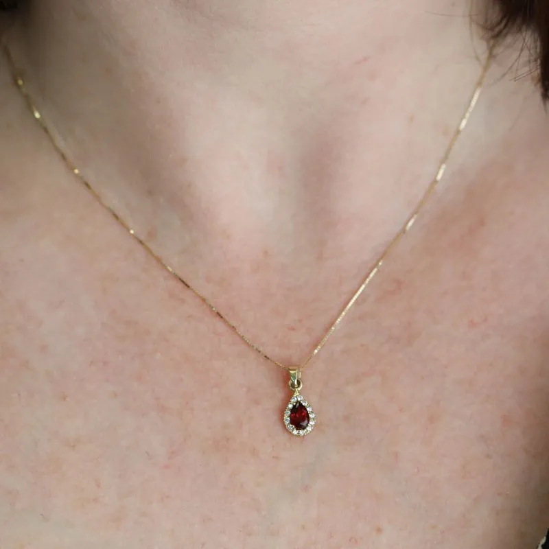 A drop-shaped halo pendant with a garnet stone on a 14K gold chain.