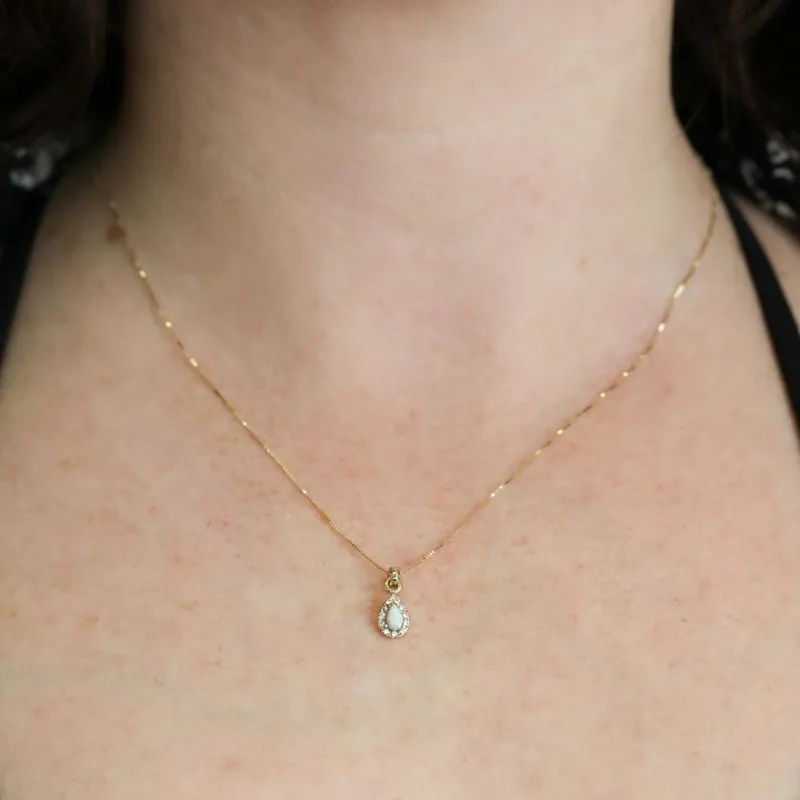 A drop-shaped halo pendant with a white opal stone on a 14K gold chain.